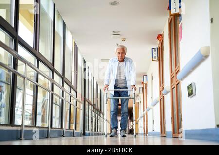 homme asiatique senior marchant à l'aide d'un marcheur dans le couloir de la maison de soins infirmiers Banque D'Images