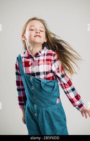 petite fille en mouvement. enfant avec air coiffure. enfant en denim costume et chemise de plaid pose en studio. photographie de mode. fond gris Banque D'Images