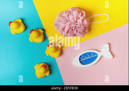 Quatre canards en caoutchouc jaune, éponge de douche et thermomètre pour l'eau sur fond bleu, rose et jaune. Concept de bain. Espace de copie, plat. Banque D'Images