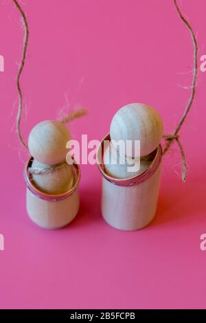 Concept d'amour malheureux. Figurines en bois avec boucles sur le cou sur un fond rose. Mari et femme sont mécontents de l'amour. Photo verticale. Banque D'Images