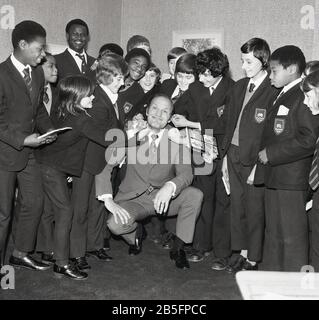 1972, historique, 'prenez-le sur le menton' .... la légende britannique de boxe Henry Cooper s'amuser avec un groupe de lycéens du sud de Londres lors d'une visite dans une école secondaire de la ville intérieure. Banque D'Images