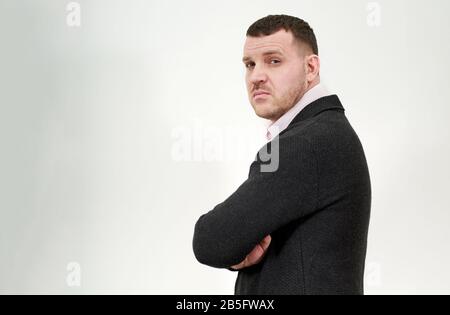 Vue latérale d'un jeune homme d'affaires élégant debout avec des bras croisés sur fond gris Banque D'Images