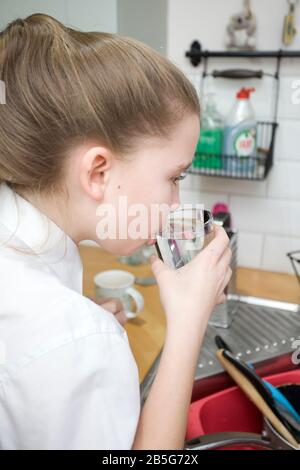 Jeune fille buvant de l'eau du robinet de l'évier de cuisine. Royaume-Uni Banque D'Images