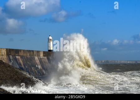 Porthcawl, PAYS DE GALLES - OCTOBRE 2018 : vagues qui s'écrasent contre le mur du port et le phare en soirée au soleil à marée haute à Porthcawl, au Pays de Galles. Banque D'Images