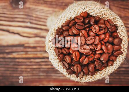 Grains de café dans un sac de burlap sur un fond en bois. Grains de café torréfiés aromatiques à contraste doux. La vue du haut. Banque D'Images