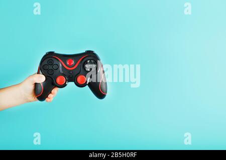 La main d'un enfant tient triomphalement la manette sur un fond bleu. Concept créatif minimaliste de la jeune génération de joueurs. Gagner en ligne Banque D'Images