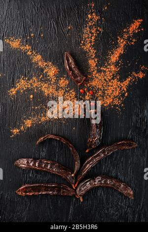 Caroub porte-fruits avec poudre sur fond noir. Sautez la poudre douce de la pulpe des gousses. Substitution de cacao et sucre, chocolat patients wi Banque D'Images