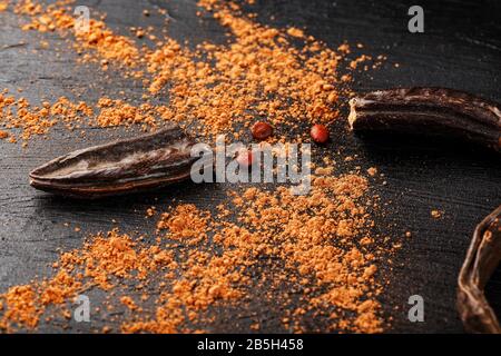 Caroub porte-fruits avec poudre sur fond noir. Sautez la poudre douce de la pulpe des gousses. Substitution de cacao et sucre, chocolat patients wi Banque D'Images