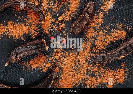 Caroub porte-fruits avec poudre sur fond noir. Sautez la poudre douce de la pulpe des gousses. Substitution de cacao et sucre, chocolat patients wi Banque D'Images