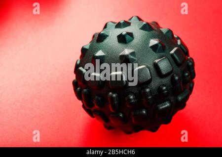 Boule de massage en mousse lumpy noire sur fond rouge. Pour les effets mécaniques et réflexes sur les tissus et les organes. Banque D'Images