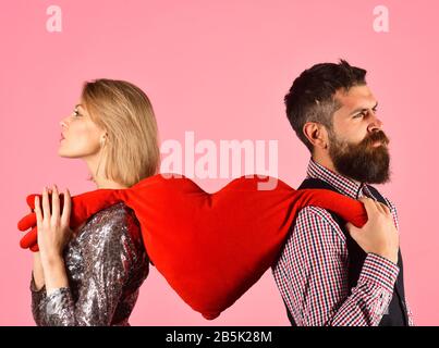 Romantisme et concept de rupture. Couple amoureux tient grand coeur sur fond rose. Fille et homme barbu avec des visages grincheux divisent le coeur doux jouet avec les mains. Petit ami et petite amie ont une pause Banque D'Images