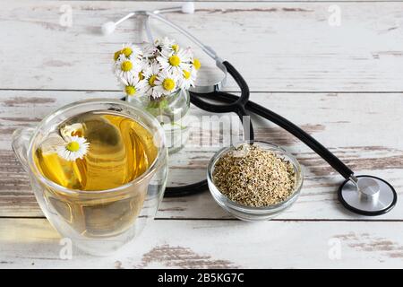 Thé camomille aux herbes dans une tasse en verre avec fleurs de camomille séchées et fraîches sur table en bois blanc. Concept de médecine alternative. Banque D'Images