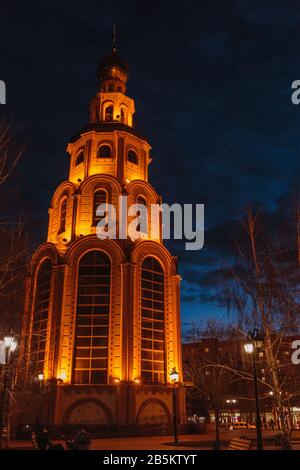 Le clocher bien mis en évidence par les lampes de poche de la ville. Une planète Vénus au-dessus d'un clocher qui brille à travers les nuages. À Krivoy Rog, Ukraine Banque D'Images