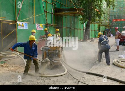 Travailleurs chargeant du sable et du ciment de mélange sec pour pompage au sommet d'un immeuble en cours de rénovation, centre est de Beijing, Chine Banque D'Images