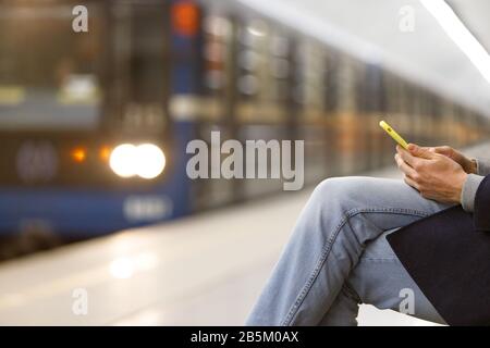 Gros plan des mains des hommes à l'aide du téléphone portable/smartphone dans un boîtier jaune au métro/station de métro, train sur fond flou, espace de copie. Ajout d'Internet Banque D'Images