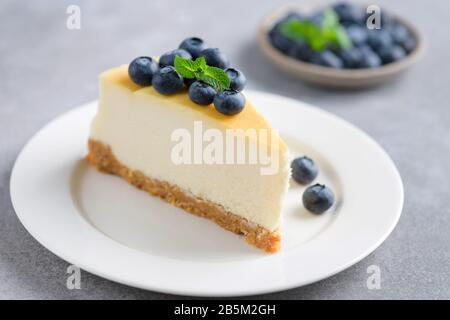 Tranche de cheesecake Uni surmontée de bleuets frais sur une plaque blanche, vue rapprochée Banque D'Images