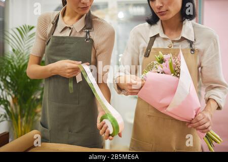 Portrait mi-section de deux fleuristes féminins décorant bouquet de tulipes roses tout en travaillant dans le fleuriste Banque D'Images