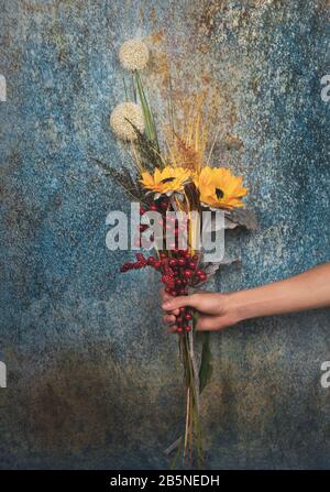 Main humaine avec un bouquet décoratif de fleurs, isolée sur un fond bleu ancien style Banque D'Images
