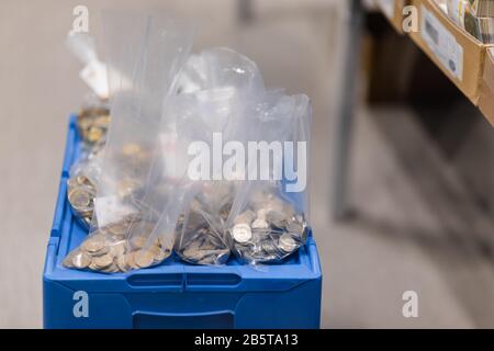 Pièces de monnaie en métal divisées en plusieurs sacs de plastique à suinter placés sur une boîte bleue Banque D'Images