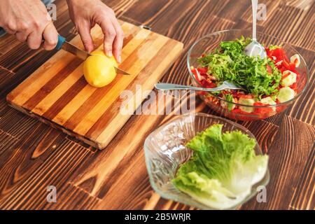La jeune femme coupe un citron sur la planche à découper pour la salade Banque D'Images