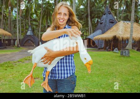 Jeune femme heureuse tenir dans les mains drôle animal de ferme - grande oie blanche domestique. Banque D'Images