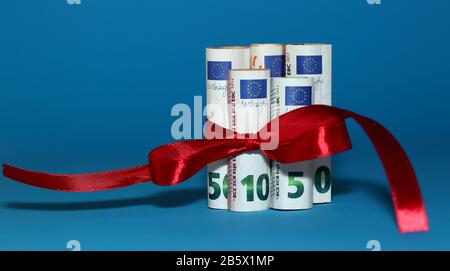 Billets de 50, 10 et 5 euros roulés en rouleaux attachés avec noeud décoratif en ruban rouge près isolé sur fond bleu, concept de cadeau économique Banque D'Images