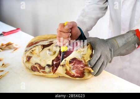 Boucherie avec un couteau tranchant court, désossage de la viande de jambon prosciutto, à l'aide d'un gant résistant à la coupe en maille de fil Banque D'Images