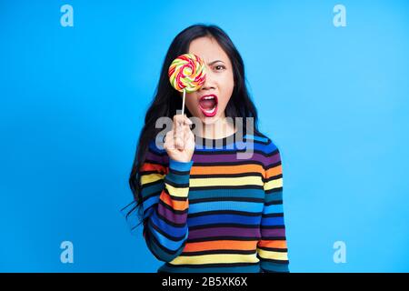 Une femme choquée qui hurle couvre ses yeux avec une pop colorée isolée sur fond bleu. Émotions, concept de la nourriture douce Banque D'Images