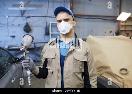 Taille vers le haut portrait d'un peintre de voiture masculin non reconnaissable portant un uniforme et un masque respiratoire sur le visage tenant pistolet spray regardant l'appareil photo, espace de copie Banque D'Images