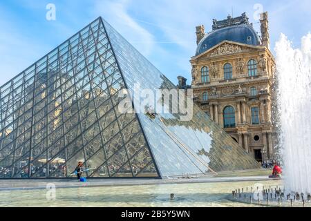 France, Paris. Journée ensoleillée d'été dans la cour du musée du Louvre. Lavage manuel et automatique de la pyramide de verre. Fontaine et touristes Banque D'Images
