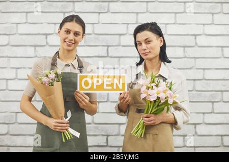 Taille en haut portrait de deux fleuristes féminins tenant UN panneau OUVERT et souriant à l'appareil photo tenant de beaux bouquets de printemps Banque D'Images