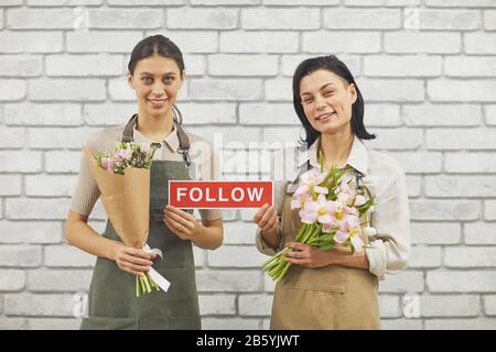 Taille vers le haut portrait de deux fleuristes féminins tenant LE panneau DE SUIVI et souriant à l'appareil photo tenant de beaux bouquets de printemps Banque D'Images