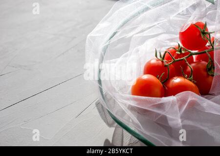 Le sac à filet organza réutilisable pour faire du shopping avec des tomates sur fond gris. Concept d'absence de plastique, zéro déchet, durée de vie réutilisable. Espace de copie. Banque D'Images