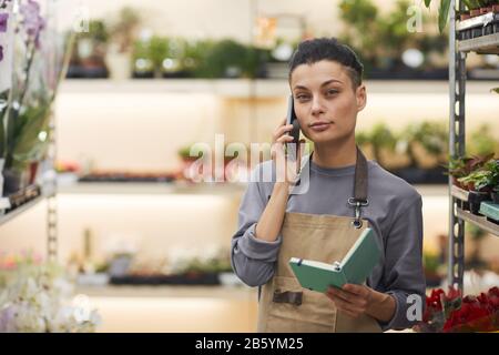 Taille vers le haut portrait de la femme réussie propriétaire d'affaires parlant par smartphone tout en se tenant dans le magasin de fleurs, espace de copie Banque D'Images