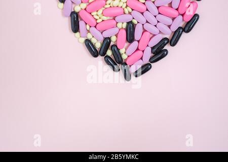 Pilules colorées dispersées en forme de coeur de produits pharmaceutiques sur un fond rose. Antibiotiques capsule antibactérienne de pilules. Idée créative. Médecine. Médicaments. Banque D'Images