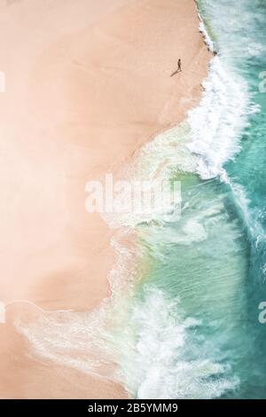 Vue imprenable sur une personne marchant sur une belle plage baignée par une mer turquoise au coucher du soleil. Plage De Kelingking, Nusa Penida, Indonésie. Banque D'Images