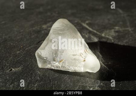 Pierre gemme de topaz blanc brut et non coupée sur fond gris ardoise , éclairée par le soleil Banque D'Images