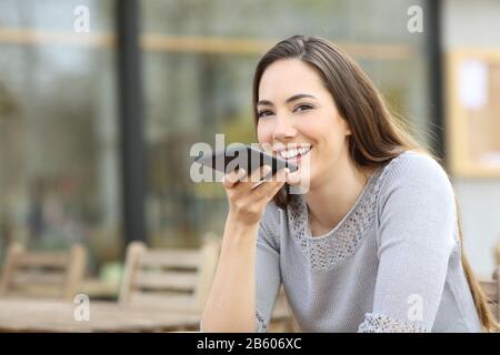 Heureuse femme utilisant le système de reconnaissance vocale sur son smartphone sur une terrasse de café Banque D'Images