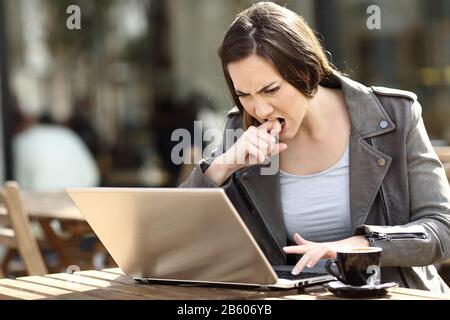 Une fille en colère appuyant sur le bouton frustrée d'utiliser son ordinateur portable sur une terrasse de café Banque D'Images