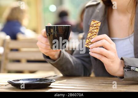 Près des mains d'une femme tenant un snack-bar à céréales et une tasse de café sur une terrasse de café Banque D'Images