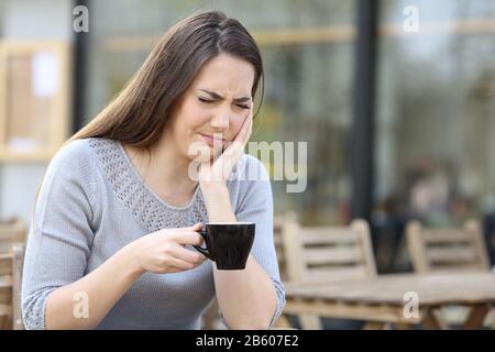 Femme souffrant d'une douleur douloureuse aux dents et tenant une tasse de café sur une terrasse de restaurant Banque D'Images