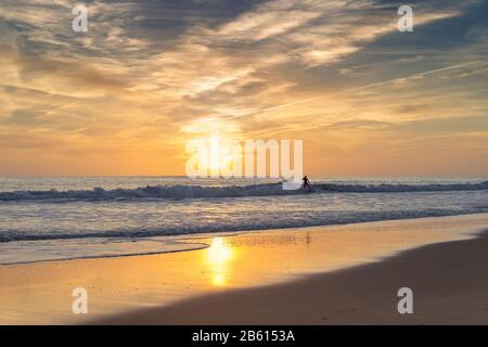 Surfer dans la mer, sur un fond des promenades au coucher du soleil. Portugal Algarve Banque D'Images