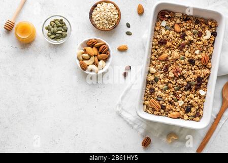 Granola maison avec des noix et des graines sur la plaque de cuisson avec des ingrédients. Granola pour un petit déjeuner sain sur blanc, vue de dessus, espace de copie. Banque D'Images