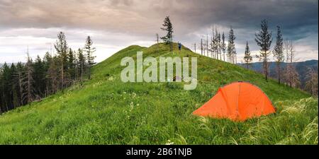 Tente de randonnée orange au sommet de la colline sous l'herbe fraîche, concept de loisirs en plein air d'été Banque D'Images