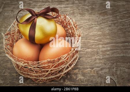 Oeufs de Pâques avec ruban brun dans un nid sur une texture en bois. Banque D'Images