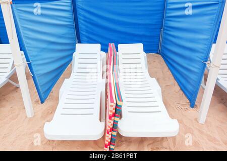 Chaises longues sur le sable, et escrime pour le vent. Banque D'Images