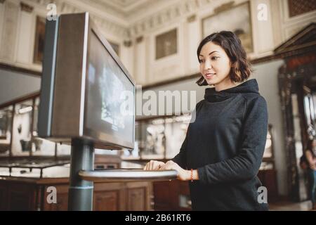 La femme utilise un moniteur moderne interactif dans le concept des musées, des technologies éducatives Banque D'Images