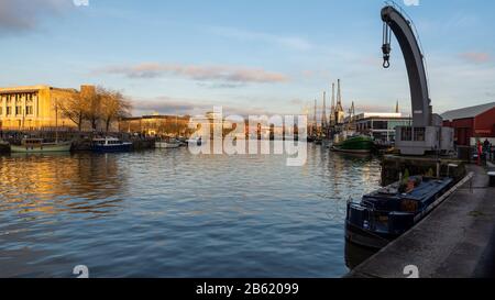 Bristol, Angleterre, Royaume-Uni - 29 décembre 2019 : le soleil du soir brille sur les bateaux, les grues et les entrepôts convertis sur les anciens docks de Bristol. Banque D'Images