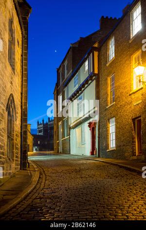 Durham, Angleterre, Royaume-Uni - 29 janvier 2017 : la cathédrale de Durham se trouve derrière des cottages traditionnels et une rue pavée la nuit. Banque D'Images