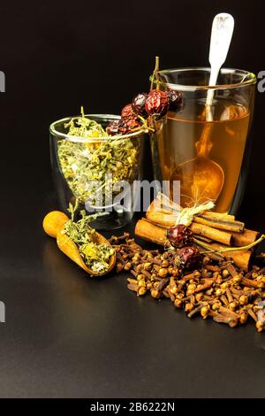 Tasse de tisanes. Divers ingrédients de tisanes dans des pots de verre sur fond noir. Médecine traditionnelle contre la grippe et le froid. Banque D'Images